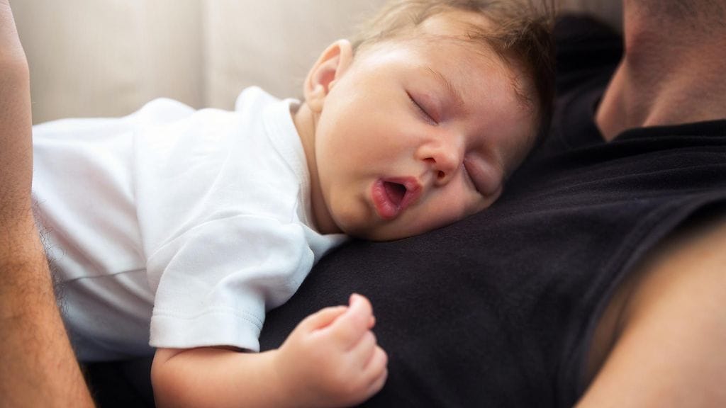 vauva nukkuu isän sylissä