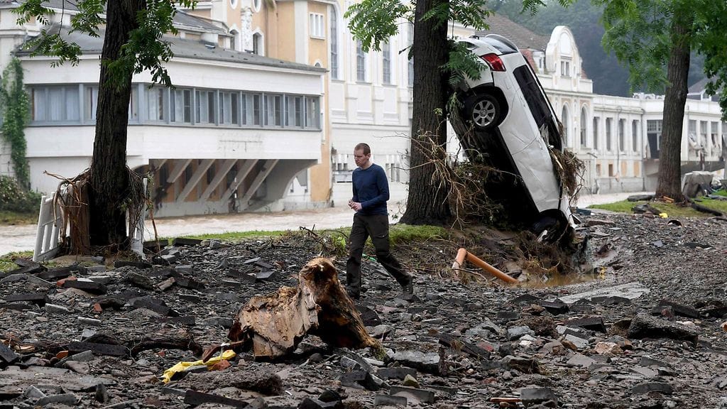 Mies kävelee tulvissa tuhotuneen auton ohi Saksassa.