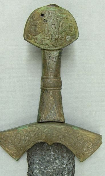 Kulahtanut miekan pronssikahva. Alareunassa näkyy kaksiteräisen rautamiehan tyviosaa.
