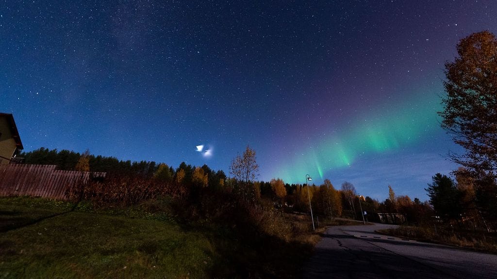 Valkoinen pallo yötaivaalla, revontulia ja tähtiä. Ilmiön aiheutti Atlas V -kantoraketti.
