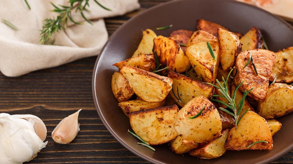 Valkosipulilla maustetussa oliiviöljyssä paistetut pehmeät perunat rapeutuvat pannulla täydellisiksi.