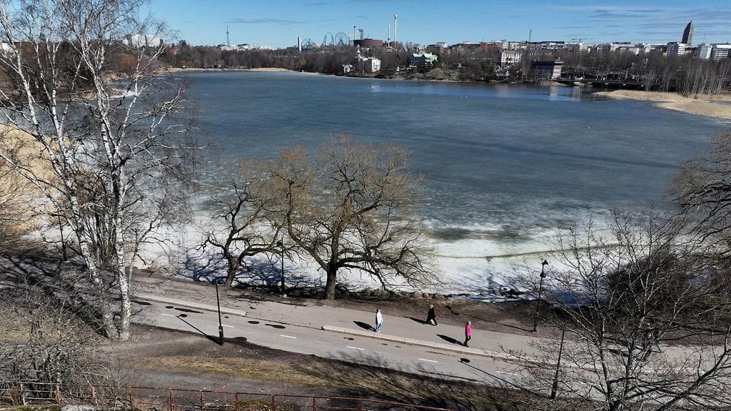 Ihmisiä kävelemässä Hesperian puistossa Helsingissä eilen tiistaina. Taustalla näkyy vielä osittain jäässä oleva Töölönlahti.