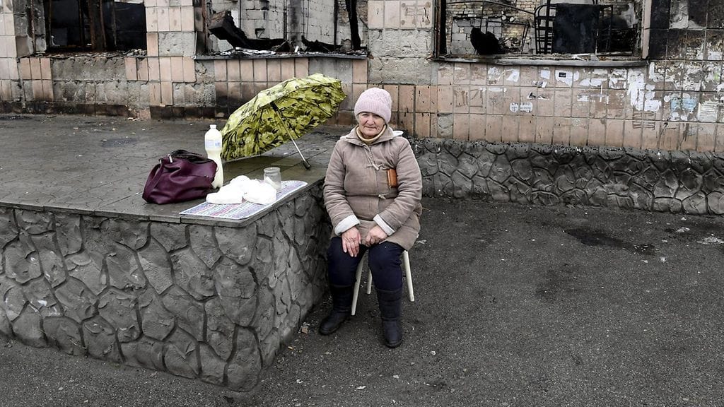 Tetiana Koronik, 70v, myy maitoa ja juustoja tuhoutuneen rakennuksen edustalla Makarivin torilla.