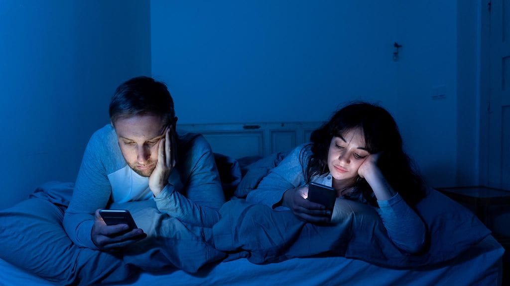 pariskunta selaa puhelimiaan sängyssä