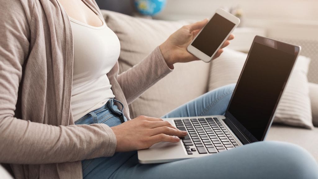 nainen tietokoneella kännykkä kädeässä