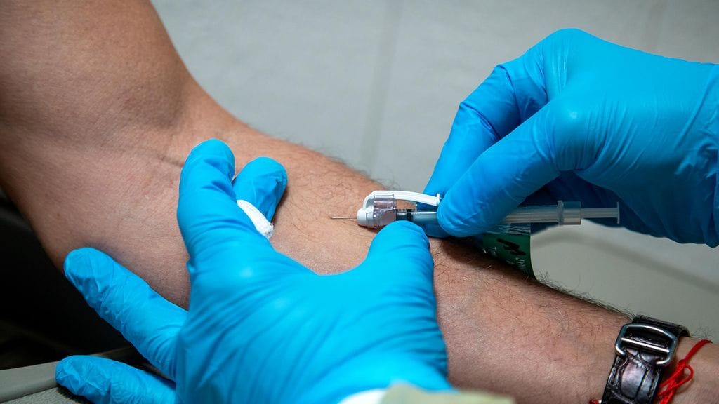 Apinarokon oireita ovat muun muassa kova päänsärky, ihottuma ja imusolmukkeiden turpoaminen. Kuvituskuva apinarokotteen antamisesta.