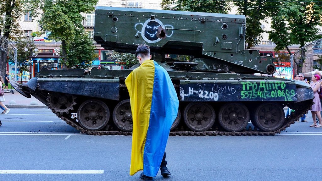 Ukrainan lippuun sonnustautunut kiovalainen tuhotun ja töhrityn venäläistankin edessä.