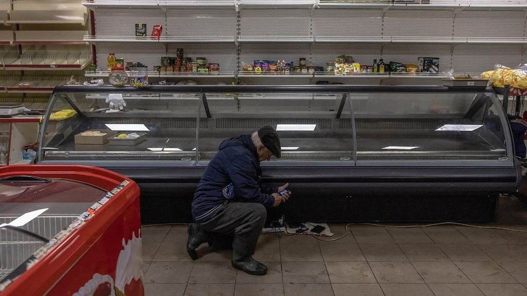 Mies latasi kännykkäänsä supermarketin lähes tyhjien hyllyjen edessä Hersonissa 26. marraskuuta 2022.