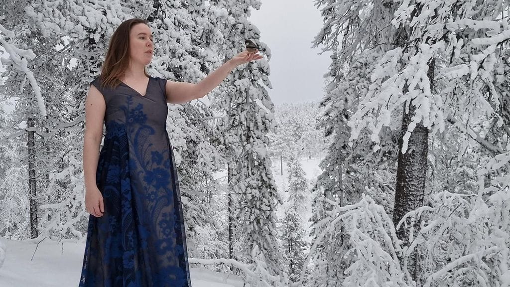 Leena Leppälä kuvattuna juhla-asussa Auroran päivätuvan pihalla Urho Kekkosen kansallispuistossa. Kuvanottohetkellä lapintiainen lennähti Leppälän päälaelle istumaan.