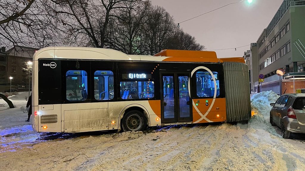Oranssi HSL:n haitaribussi taittuneena jumissa lumisella kadulla.