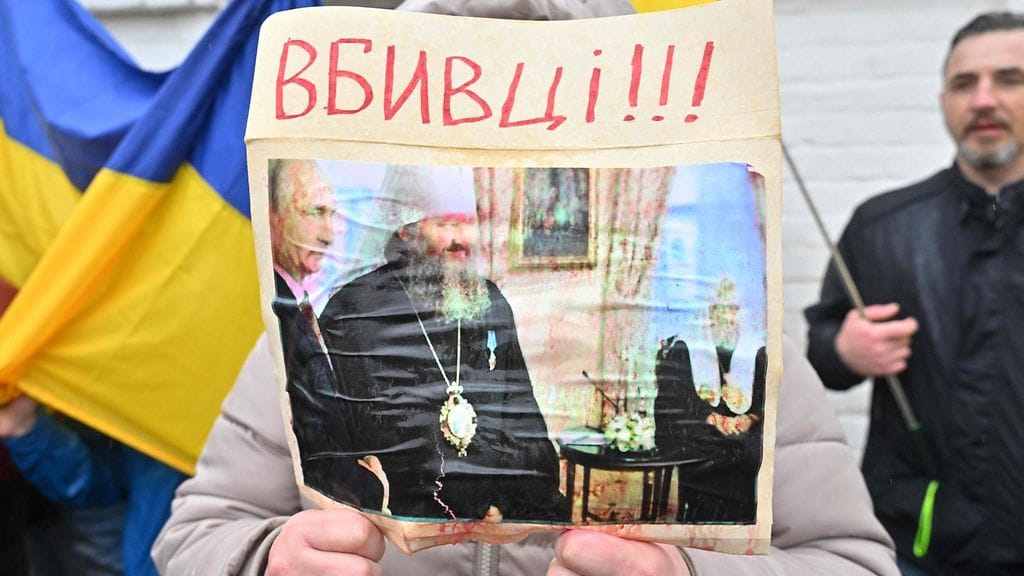 Nainen pitelee kuvaa, jossa metropoliitta Pavlo seisoo Venäjän presidentin Vladimir Putinin vieressä. Kuvassa heitä kutsutaan tappajiksi.