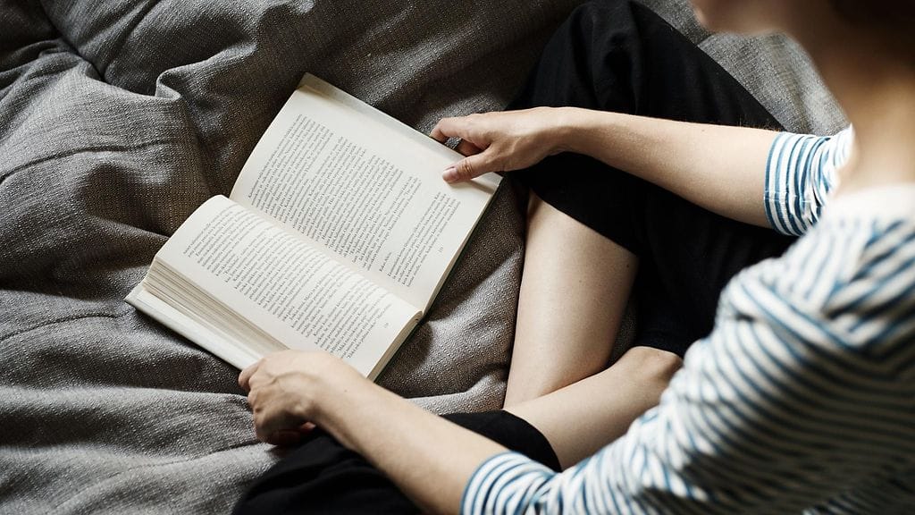 Suomalaiset kertovat käyttävänsä enemmän aikaa kirjojen lukemiseen ja kuunteluun kuin internetin viihdekäyttöön, selviää tuoreesta Suomi lukee -tutkimuksesta. Kuvituskuvan nainen luki kirjaa kotonaan 16. elokuuta 2019.