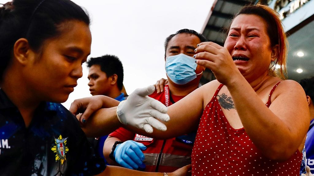 Punatoppinen nainen itkee auttajien antaessa tukea.