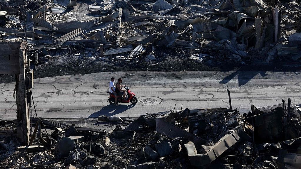 Kaksi miestä ajavat skootterilla palaneiden rakennusten keskellä Havaijilla 11. elokuuta 2023.