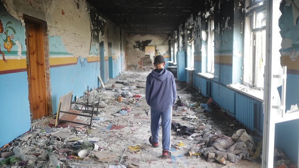 13-vuotias poika kävelee rypälepommien tuhoamassa koulussa Itä-Ukrainan Lymanissa heinäkuussa 2023.