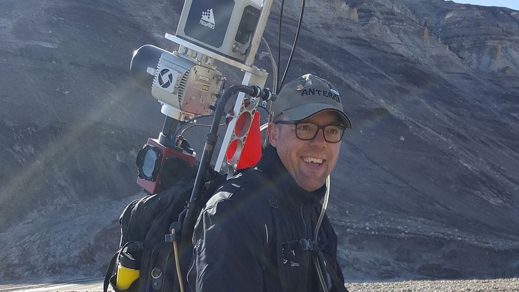 Maanmittauslaitoksen Paikkatietokeskuksen tutkimusprofessori Antero Kukko tutkimustyössä Axel Heibergin saarella Kanadan arktisessa osassa. Selässä kannettavan laserkeilausrepun tuottamalla tiedolla voi tehdä tutkittavasta ympäristöstä tarkan kartan ja 3D-mallin.