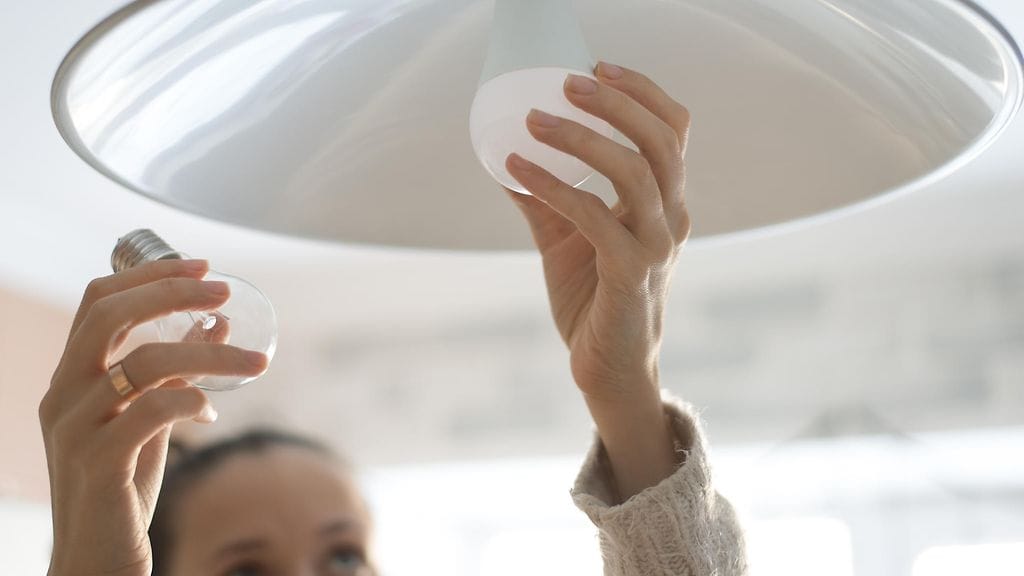 nainen laittaa lamppua paikalleen