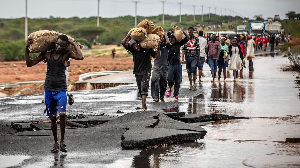 Tulville kotinsa menettäneet
ihmiset kantavat tavaroitaan ylittäessään tien osan, joka romahti äkkitulvien takia.