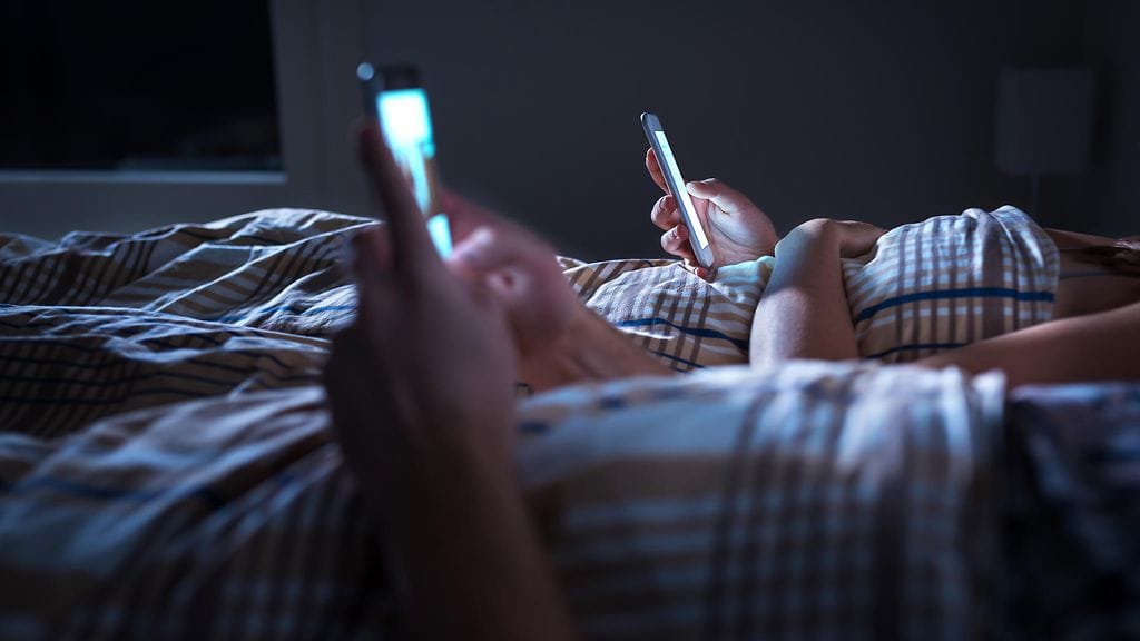 pariskunta selaa puhelimia sängyssä