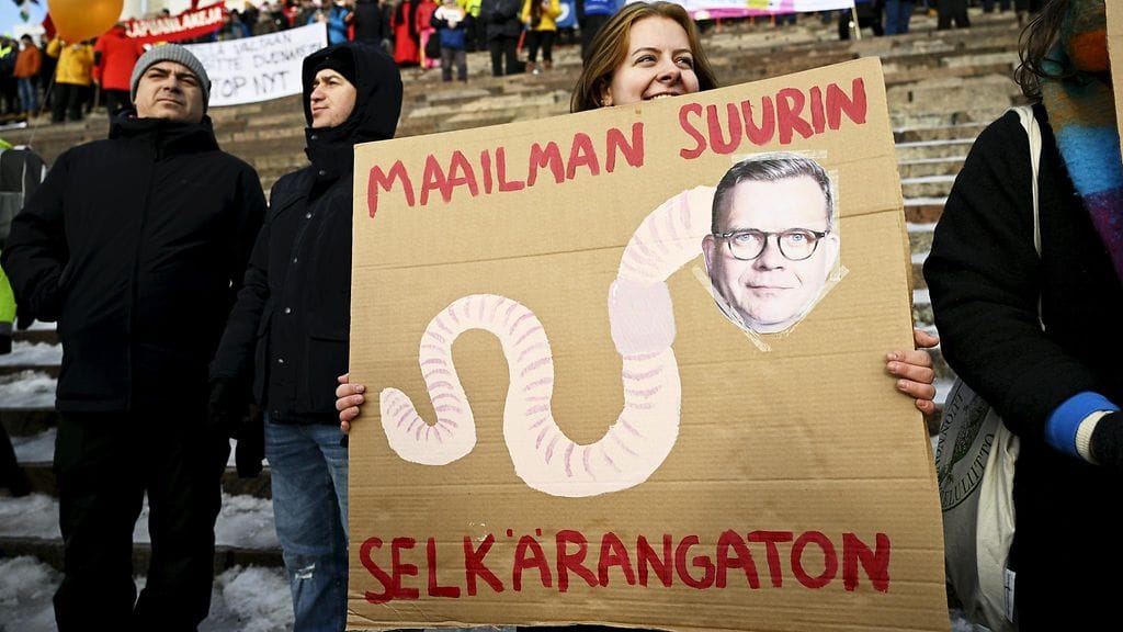 Liisa Huhtala pitelee tekemäänsä kylttiä tuomiokirkon portailla SAK:n ja STTK:n järjestämässä hallituksen suunnittelemia työelämän heikennyksiä vastustavassa Stop Nyt! -mielenosoituksessa Helsingin Senaatintorilla 1. helmikuuta 2024.