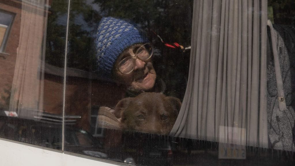 Vovtshanskin alueelta evakuoitu iäkäs nainen istuu koiransa kanssa autossa evakuointipisteessä.