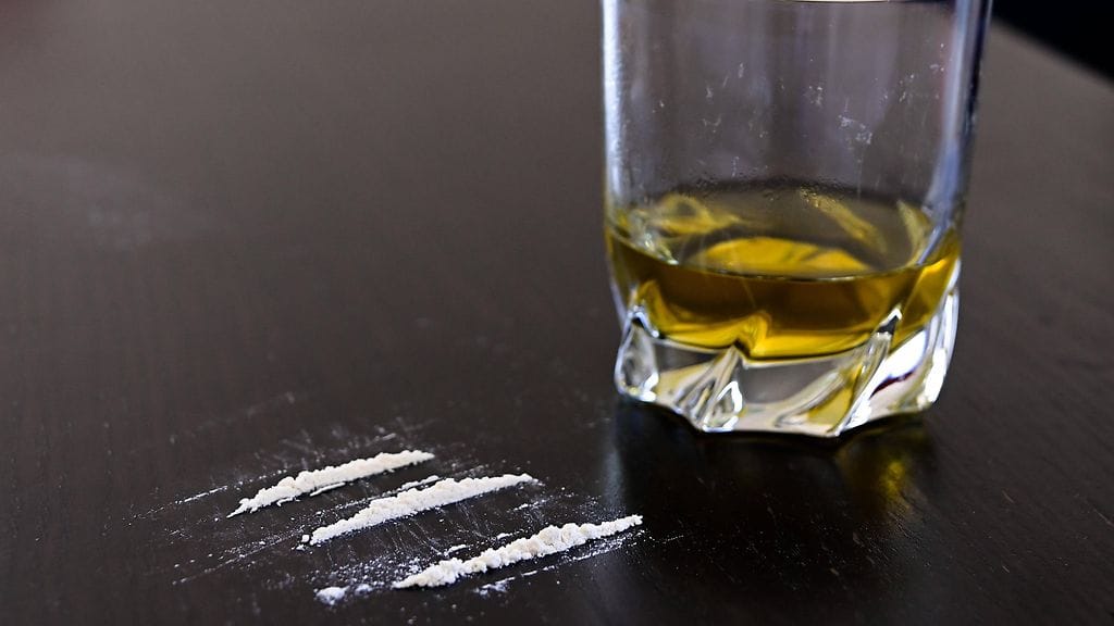 Kuvituskuva, jossa jauhemaista huumausainetta pöydällä ja lasillinen vahvaa alkoholia.