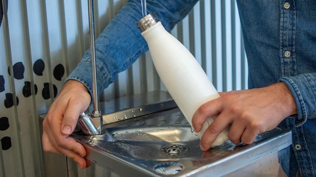 AOP Nuori mies täyttää vesipulloaan lentokentän vesiautomaatista.