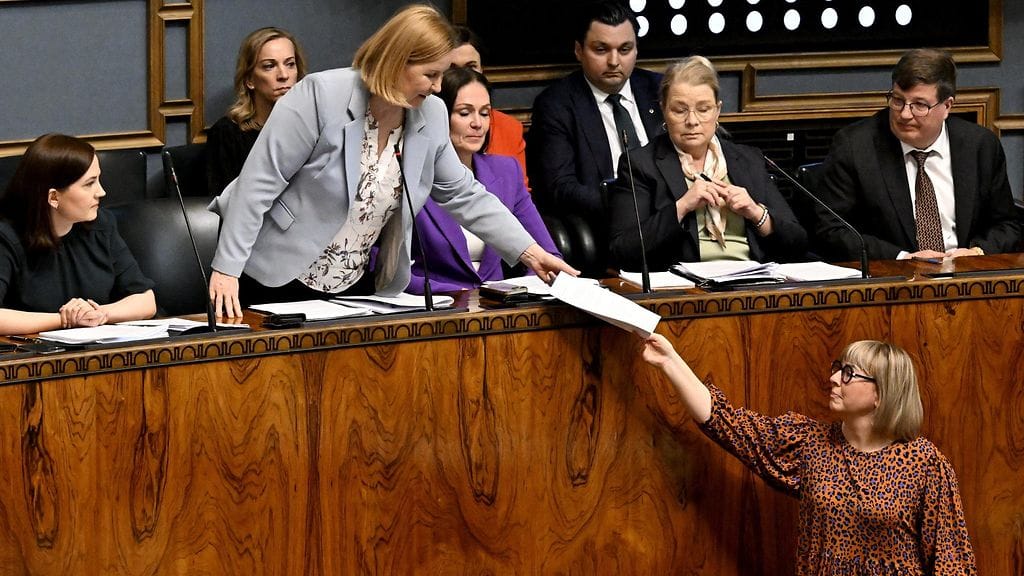 Sosiaali- ja terveysministeri Kaisa Juuso (ps.) luovuttaa sosiaalihuollon säästöjä käsittelevän asiakirjan vasemmistoliiton kansanedustajalta Aino-Kaisa Pekoselta eduskunnan suullisella kyselytunnilla Helsingissä 3. huhtikuuta 2025.