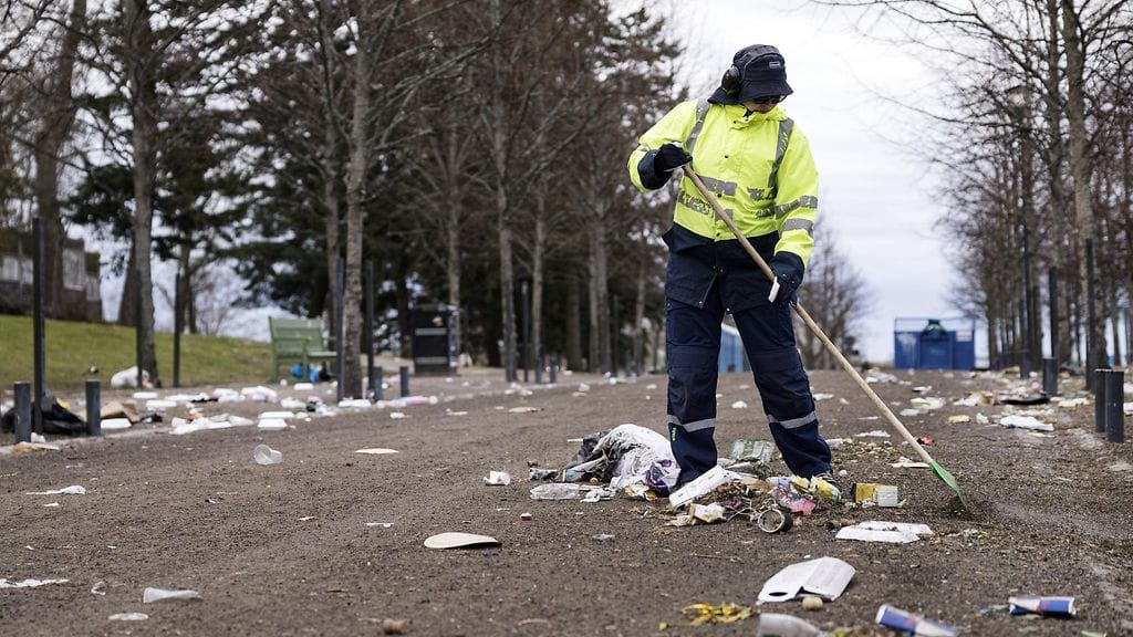 Huomioliivinkeltaiseen takkiin sonustautunut siivooja haravoi roskaista hiekkatietä Kaivopuistossa.