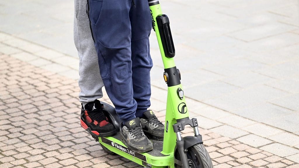 Kaksi nuorta skuuttailemassa vappupäivänä samalla sähköpotkulaudalla.