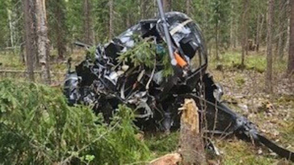 Täysin tuhoutunut helikopteri makaa katkenneen puun vieressä keskellä metsää.