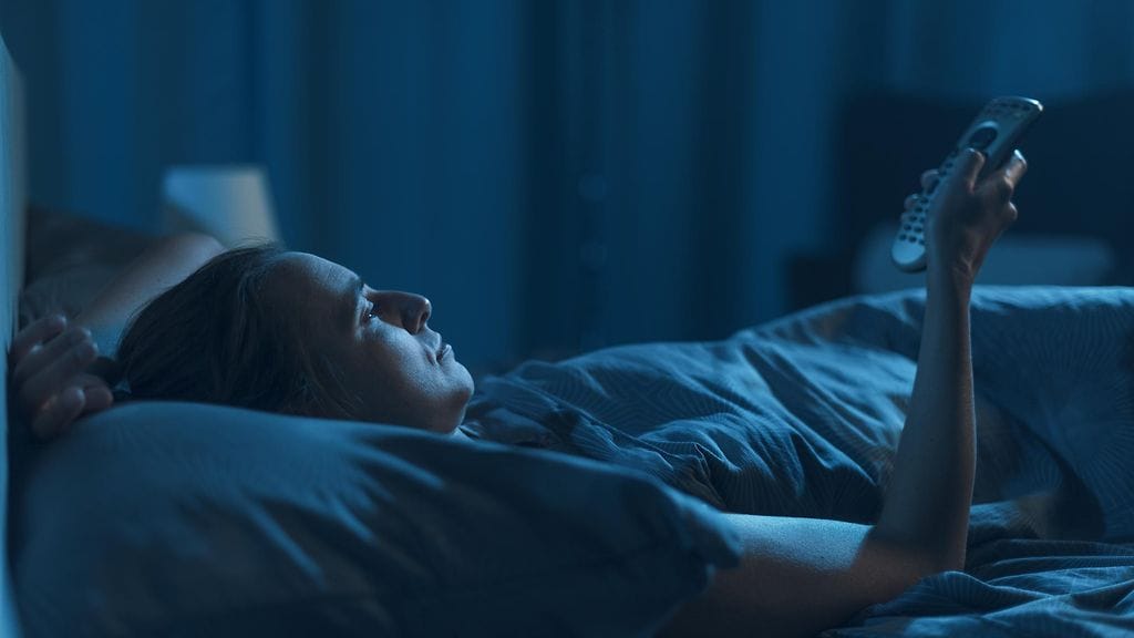 nainen katsoo sängyssä televisiota