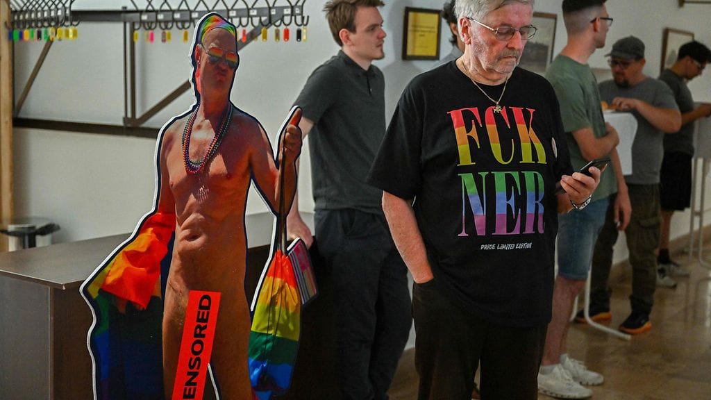 Mies selaili puhelinta Fidesz-puoluetta kritisoiva t-paita yllään Budapestin kaupungintalolla keskiviikkona. Hänen vierellään on puolueen kannattajien asettama pahvikuva alastomasta miehestä sateenkaarilipun kanssa.