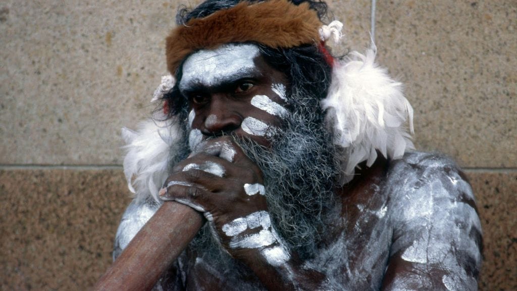 Alkuperäiskansaan kuuluva mies soittaa didgeridoo-soitinta kadulla Australiassa.