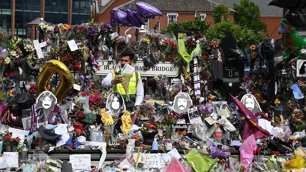 Mies seisoo ruusu- ja lahjavuoren keskellä Ozzy Osbournen hautajaiskulkuetta varten järjestyssä kokoontumisessa.