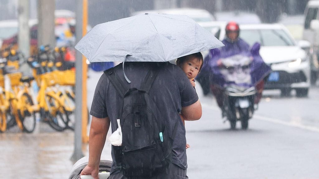 Henkilö pitelee vauvaa sylissään tiellä sateen keskellä Pekingissä 4. elokuuta 2025