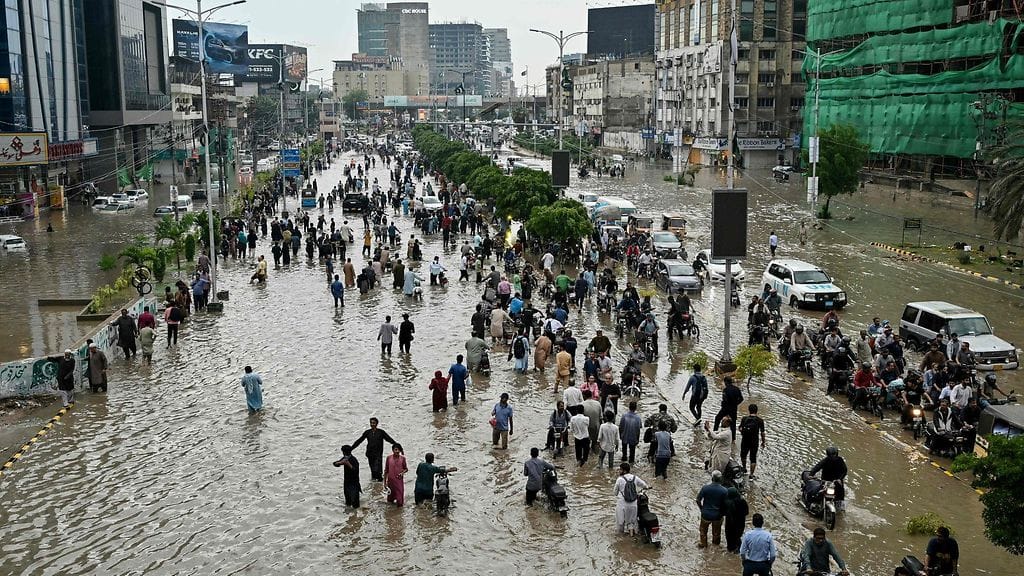 Ihmiset kahlasivat tulvivan kadun läpi rankkasateiden jälkeen Karachissa 19. elokuuta 2025.