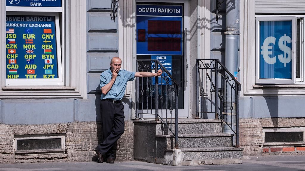 Mies poltti tupakkaa valuutanvaihtopisteen edessä Moskovassa kesäkuussa 2024.