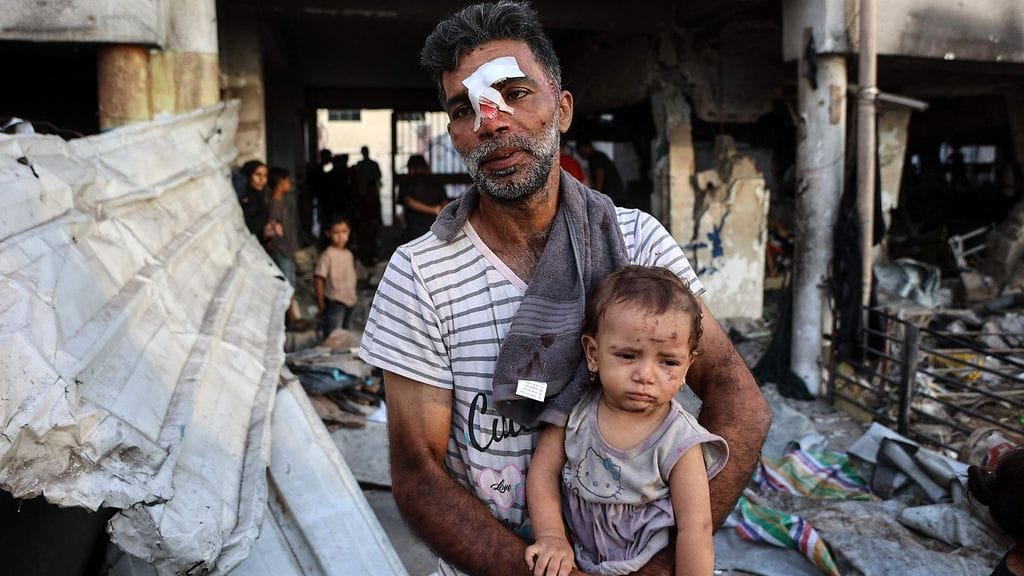 Loukkaantunut mies kantoi pientä lasta Israelin iskettyä suojapaikkana toimineeseen al-Farabin kouluun Gazan kaupungissa 7. syyskuuta 2025.