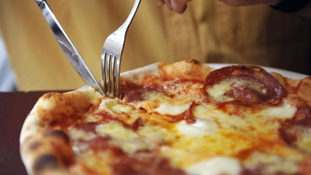 Henkilö syömässä salamipizzaa ravintolassa. Kuvituskuva.