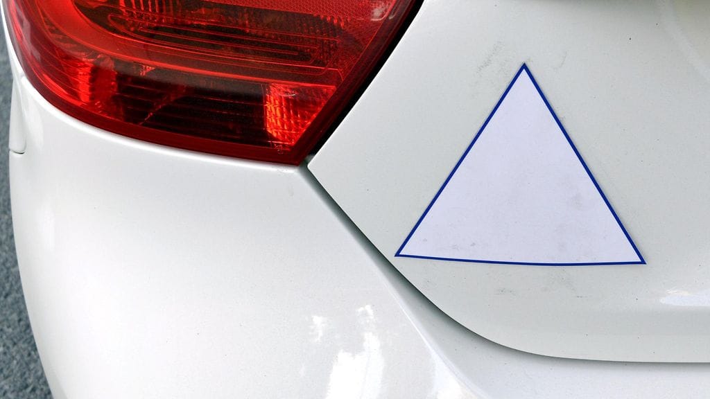 Ajoharjoittelusta kertova valkoinen kolmio autossa.