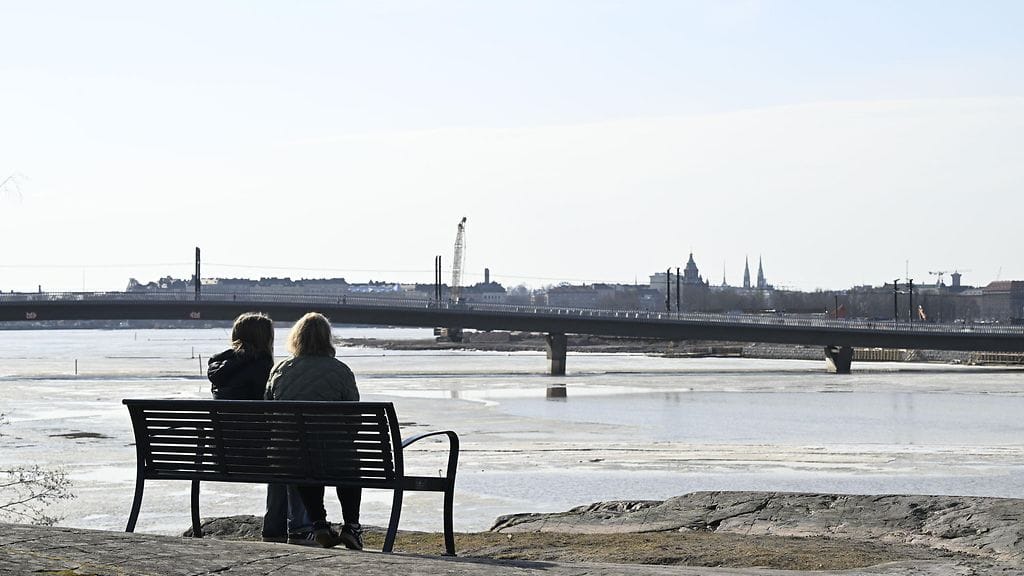 Ihmiset paistattelevat päivää keväisessä plussakelissä Helsingissä 15. maaliskuuta 2026. Taustalla Kruunusiltojen Finkensilta.